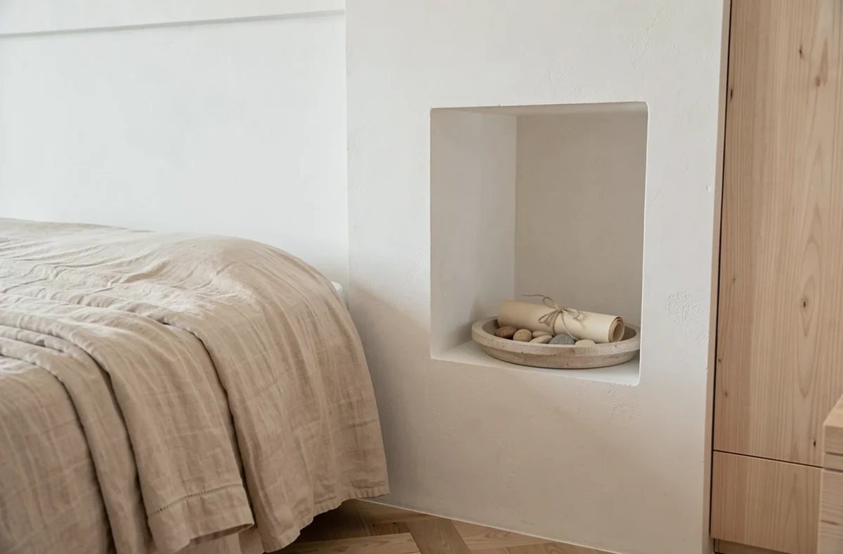 Chambre minimaliste avec literie beige en coton percale, niche en plâtre blanc et détails déco en lin et grès sur parquet chêne