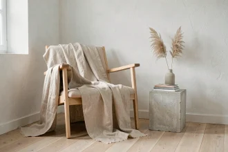Coin salon minimaliste avec fauteuil en chêne pâle, plaid beige en lin et vase céramique sur table en béton brut dans un intérieur épuré